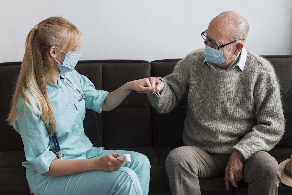 A homecare worker and her elderly client in conversation while wearing facemasks.