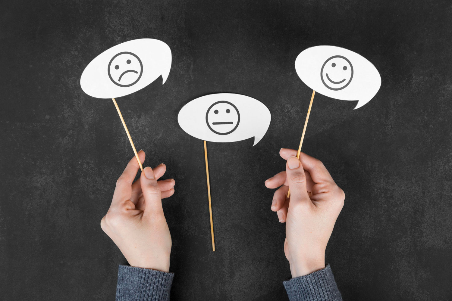 Someone holding up three speech bubbles. One with a sad face, one with an undecided face and one with a happy face. 